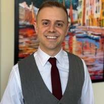 Man, Gray Vest, Maroon Tie standing in front of a painting