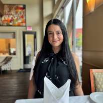 Woman Long Dark Hair, black shirt standing behind a table