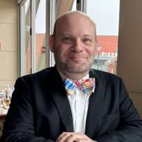 Man, Black Suit, White Shirt, Bowtie Standing behind chairs