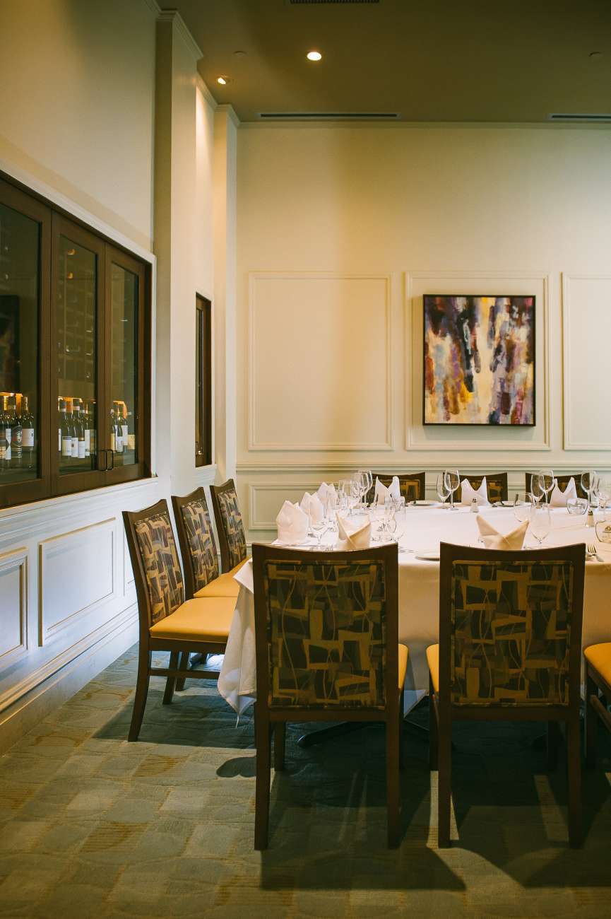 The Wine Room shown with a large square table for 12. The Davio's wine collection is visible along one wall, and an abstract painting is above the table on another wall.